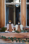 Cinnamon-stick angels, tealights and ivy in rustic window