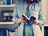 Frau in Jeanshemd mit Buch vor Bücherregal