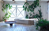 Fur blanket on couch in bright room with wooden floor and many houseplants
