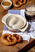 Munich Bavarian traditional white sausages in ceramic pan served with german sweet mustard, mug of dark beer and pretzels