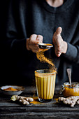A person holding a glass of golden milk with turmeric ginger and honey