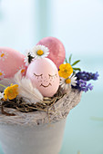 Pot as a decorative Easter basket with an Easter egg with a drawn face, daisies, buttercups, grape hyacinth, and feather