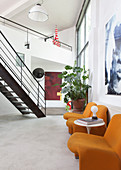 Orange chairs and a side table in a loft apartment with stairs in the background