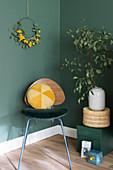 Gelbes Samtkissen auf einem Retro-Stuhl vor dunkelgrüner Wand