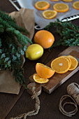 Sliced oranges on chopping board next to evergreen branches