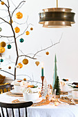Branch decorated with yellow and petrol baubles on set table