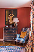 An upholstered armchair, a chest of drawers and 1930s Art Deco-style artwork