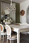 A white shabby chic-style dining table and medallion chairs in front of a wall mirror in a dining room