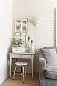 A shabby chic-style drawer table and a stool against a white-painted brick wall