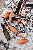 Sweet potatoes cooking in the embers of a barbecue fire