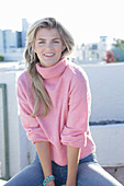 A young blonde woman wearing a pink turtle-neck jumper