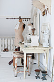 A statue and plants on a white, shabby-chic style table in front of a dressmaker's dummy