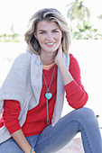 A young blonde woman wearing a red jumper with a light-coloured jumper over her shoulders