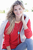 A young blonde woman wearing a red jumper with a light-coloured jumper over her shoulders