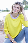 A young blonde woman wearing a yellow jumper and jeans