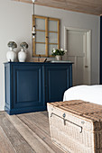 Rattantruhe am Bett und blaues Sideboard im Schlafzimmer