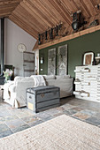 A wooden chest behind a sofa and an armchair in an open-plan living room in a former farmhouse