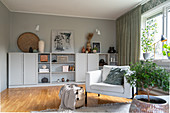 A light upholstered armchair in a living room with a grey highboard in front of a grey wall