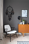 An armchair, a dream catcher and a sideboard in front of a dark wall in a bedroom