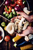 A hand holding oyster mushrooms above fresh vegetables