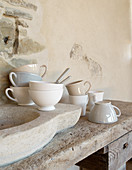 Cups in natural shades on rustic sink next to stone wall
