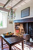 Chandelier above wooden table in rustic kitchen with wood-burning stove