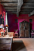 Antique wooden furniture and wood-beamed ceiling in room with purple wall