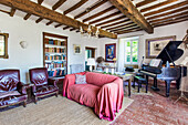 Piano, sofa and leather armchairs in country living room with wood-beamed ceiling