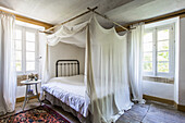 Bett mit Vorhang im Schlafzimmer mit rustikaler Holzdielenboden
