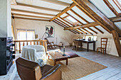 Armchair and wooden table in rustic attic bedroom with wood-beamed ceiling