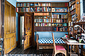 Wooden bookshelves above daybed with desk in study