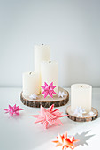 White pillar candles on wooden discs with origami 3D stars
