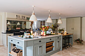 Cream pendant lights hang above marble-topped island unit in Regency farmhouse kitchen