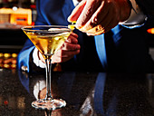 A cocktail being garnished with lemon zest