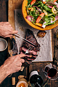Grilled tomahawk steak on a wooden board with salad being served