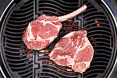Raw tomahawk steak and porterhouse steak on a grill rack