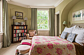Pink floral quilted cover on bed in Victorian home with vintage bookcase