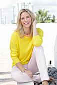 A blonde woman wearing a yellow jumper and white trousers