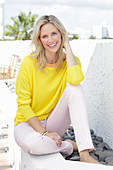 A blonde woman wearing a yellow jumper and white trousers