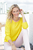 A blonde woman wearing a yellow jumper and white trousers