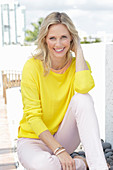 A blonde woman wearing a yellow jumper and white trousers