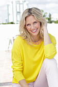 A blonde woman wearing a yellow jumper and white trousers