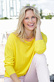 A blonde woman wearing a yellow jumper and white trousers