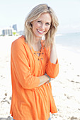 A blonde woman by the sea wearing an orange tunic