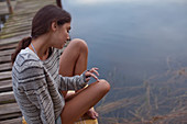 Pensive woman sitting on dock over lake