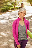 Older woman carrying yoga mat outdoors