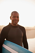 Older surfer carrying board on beach