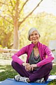 Older woman sitting on yoga mat outdoors