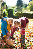 Girls petting dog in autumn leaves