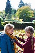 Girl tying sister's scarf outdoors